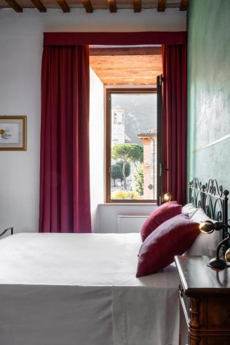 a bedroom with a white bed with red curtains and a window at Hotel San Marco in Gubbio