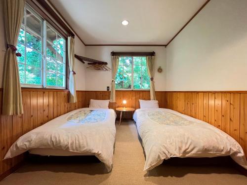 2 Betten in einem Zimmer mit 2 Fenstern in der Unterkunft Pension Alps Hakuba in Hakuba