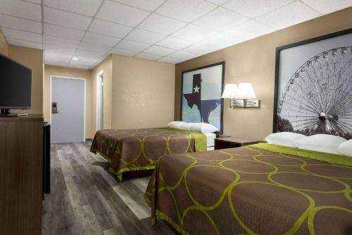 a hotel room with two beds and a flat screen tv at Super 8 by Wyndham Gainesville TX in Gainesville