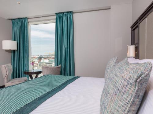 a bedroom with a bed and a window with green curtains at Grand Central Hotel Belfast in Belfast