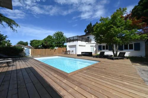 une cour arrière avec une piscine et une terrasse en bois dans l'établissement Villa Le Chêne Vert, à Arès