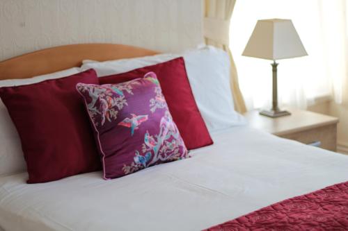a white bed with red and purple pillows and a lamp at Cleve Court Hotel in Paignton