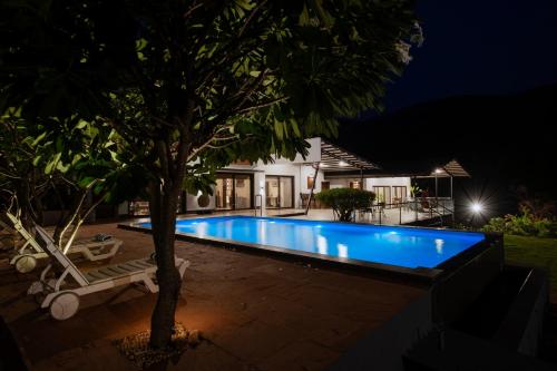 a swimming pool in a backyard at night at SaffronStays Sanvina Farm, Karjat in Karjat