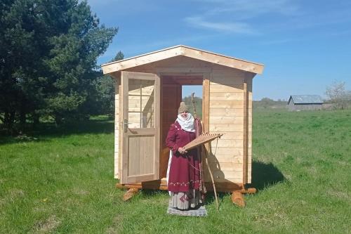 une femme debout devant une maison extérieure en bois dans l'établissement Bičių lova. Bičių terapija. Bee bed. Bee therapy, 