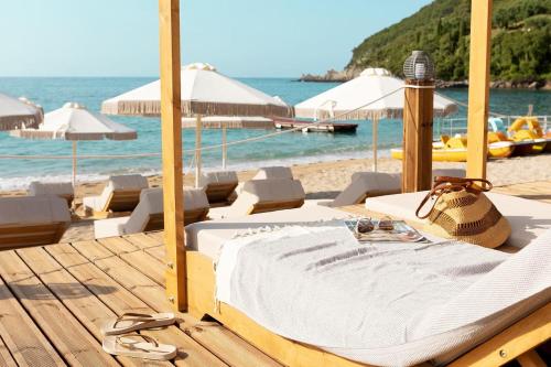 Cama en una playa con sillas y sombrillas en Enjoy Lichnos Bay Village, Camping, Hotel and Apartments en Párga