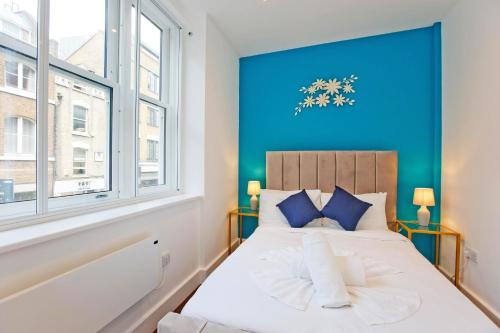 Un dormitorio con una pared azul y una cama con almohadas azules. en Imperial Middlesex Street Apartments en Londres