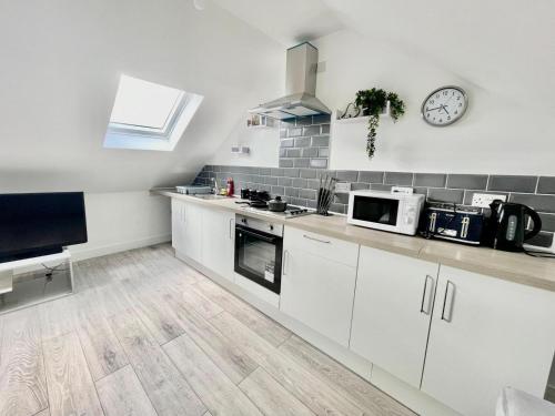 una cocina con armarios blancos y un reloj en la pared en Exec 1-Bedroom Studio Apartment Briton Ferry, Neath Port Talbot 5, en Briton Ferry