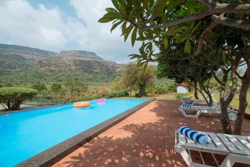 a swimming pool with chairs and mountains in the background at SaffronStays Sanvina Farm, Karjat in Karjat