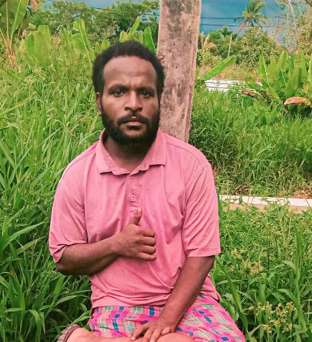 a man in a pink shirt sitting next to a pole at Gorong-gorong angkatan laut bawah in Timika