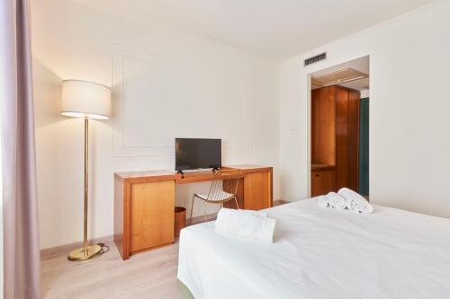 a bedroom with two beds and a desk with a television at Hotel Cyrano in Saronno