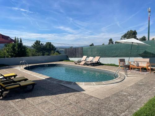 a swimming pool with chairs and a table and an umbrella at Refúgio da Légua in Marco de Canavezes