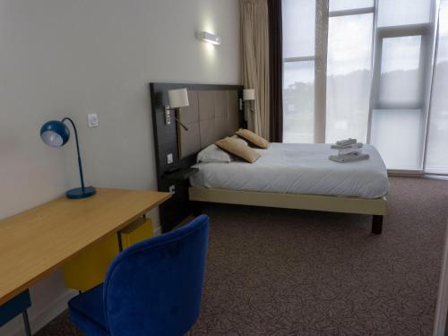 a bedroom with a bed and a desk and a blue chair at Hôtel la Verriaire - The Originals in La Verrie