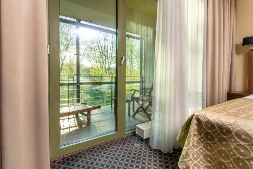 um quarto com uma cama e uma porta de vidro com uma varanda em Grand SPA Lietuva Hotel Druskininkai em Druskininkai