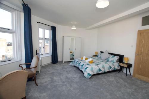 a bedroom with a bed and a chair and windows at Beautiful large 3-bed coastal flat with parking. in Frinton-on-Sea