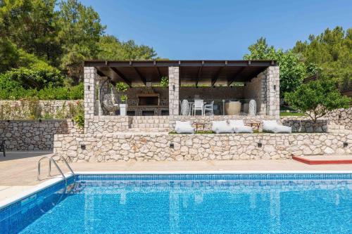 a swimming pool with a stone wall next to a house at Adonis Villa in nature in Ixia