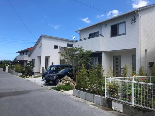 a car parked in front of a white house at 空港まで車で15分〜ビーチまで徒歩1分〜海沿いの野鶴居 in Maezato