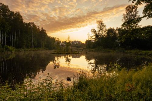 a sunset over a pond with a house in the background at Osada Skoczkowo komfortowe domki z prywatnymi wannami hot-tub nad jeziorem- sauna- balia- prywatny staw wędkarski in Podiazy