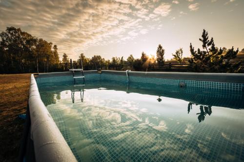 a swimming pool in a field with the sun setting at Osada Skoczkowo komfortowe domki z prywatnymi wannami hot-tub nad jeziorem- sauna- balia- prywatny staw wędkarski in Podiazy