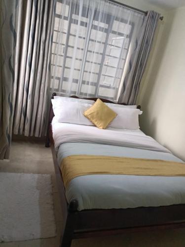 1 cama con almohada amarilla frente a una ventana en Cavendish Square - Hazz_Homes, en Syokimau