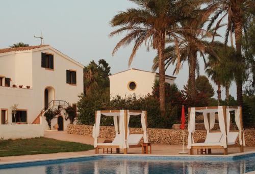 a pool with two white chairs and a house at Llucatx Menorca in Son Parc