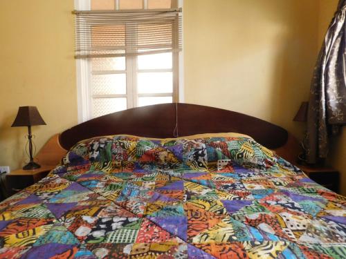 a bed with a colorful quilt on it with a window at Jesiwa B's Little Palace in Accra