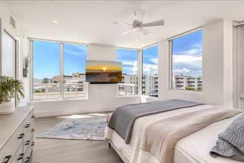 a bedroom with white walls and windows with a bed and a flat screen tv at Ten35 Seaside Rentals in Sarasota