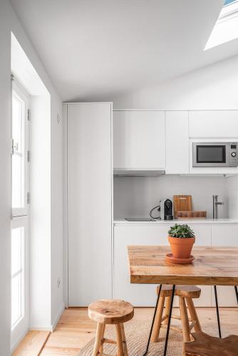 a white kitchen with a wooden table and two stools at Loureiro 59 in Coimbra