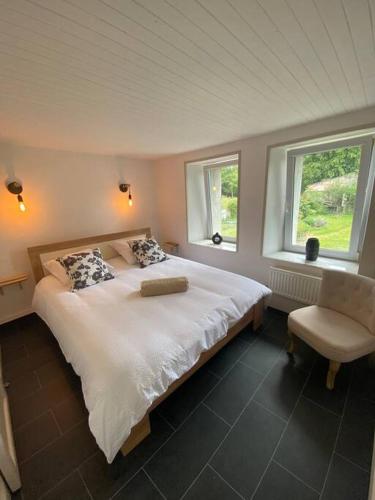- une chambre avec un lit, une chaise et deux fenêtres dans l'établissement Le gîte de l’arbre, à Hargnies