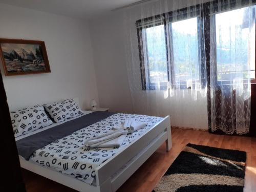 a bedroom with a bed with white sheets and windows at Apartman Petković in Višegrad