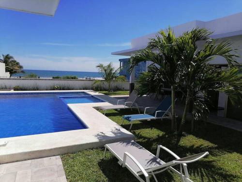 einen Pool mit Stühlen und eine Palme neben einem Haus in der Unterkunft VillaGera ¡Tu casa en la playa! in Ursulo Galván