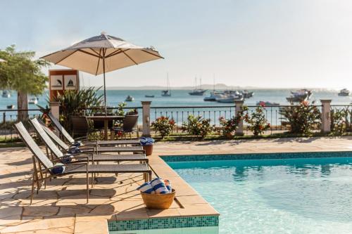 a swimming pool with lounge chairs and an umbrella at Pousada Corsario Buzios in Búzios