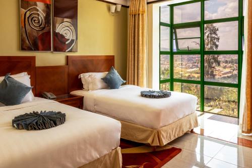 two beds in a room with a large window at Highlands Suites Hotel and Apartments in Kigali