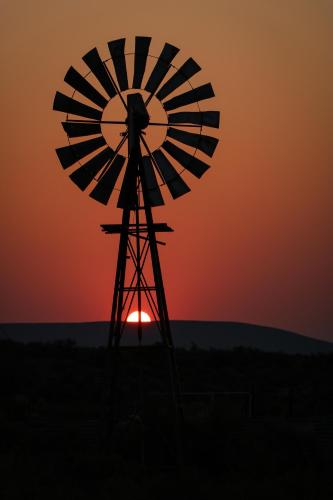 a silhouette of a windmill in front of a sunset at Oupoort Eco & Guest Farm - Sutherland - Middelpos in Sutherland