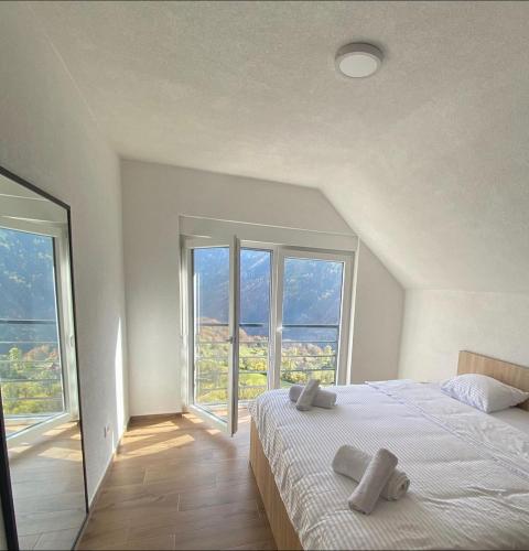 a white bedroom with a bed and large windows at Villat Twin’s in Peje