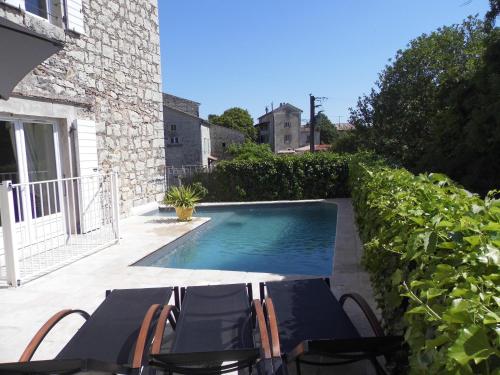 une piscine avec une table et des chaises à côté d'un bâtiment dans l'établissement La Mais'Ange, à Berrias Et Casteljau