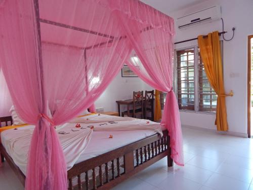 un letto con zanzariera rosa in una stanza di Rico Shadow Guest House & Restaurant a Wayikkal
