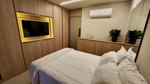a bedroom with a white bed and a flat screen tv at Loft de Luxo c/ Home Office ao lado Shopping CG. in Campo Grande
