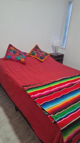 Una cama roja con una manta de colores. en Departamento cómodo en La Rioja