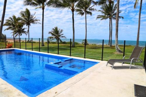 uma piscina azul com palmeiras e o oceano em Sarina Beach Motel em Sarina