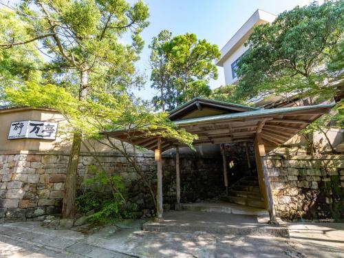 una entrada de madera a una casa con una pared de piedra en Tabist Nanki Shirahama Ryokan Mantei en Shirahama