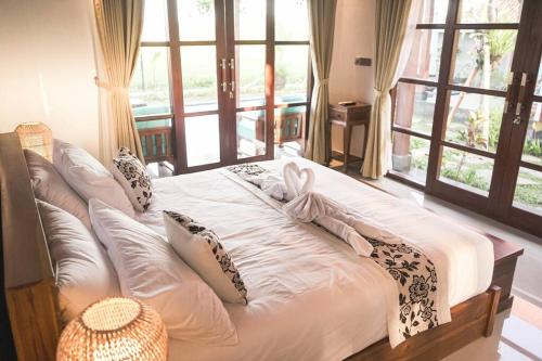 een bed met witte lakens en kussens in een kamer met ramen bij Villa Puri Kembar in Ubud