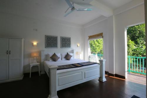 a bedroom with a white bed and a balcony at Ceylon House By Sunrise in Ella