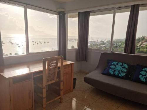 a living room with a desk and a couch and windows at chez Karine et Robert in Punaauia