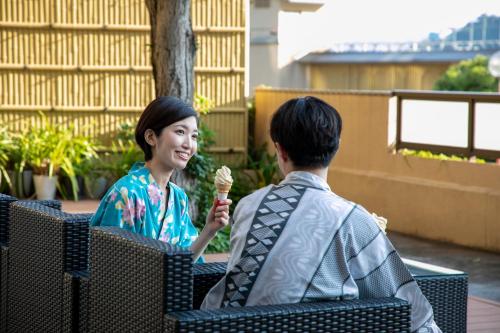 Um homem e uma mulher sentados num banco a comer gelado. em Yuyado Ichibanchi em Atami