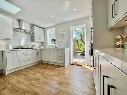 a kitchen with white cabinets and a wooden floor at Family home in Hampshire - Sleeps up to 9 people with 3 parking spaces in Winchester