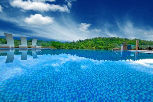 a large swimming pool with blue water and white chairs at The Golden Crown Hotel in Kandy