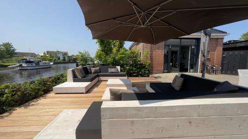 a patio with couches and an umbrella next to a river at PUUR Eastermar - monumentaal, authentiek en luxe koetshuis aan open vaarwater met jacuzzi en sauna in Oostermeer