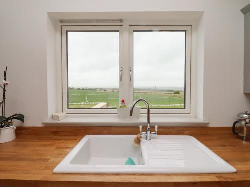 a white sink in a kitchen with two windows at Cotswold View in Chipping Norton
