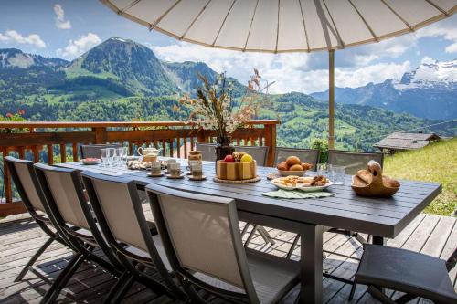 a table with food and an umbrella on a deck with mountains at Chalet Chenavray - OVO Network in Manigod