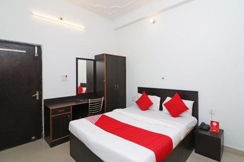 een slaapkamer met een bed met rode kussens en een bureau bij OYO Flagship 24199 Hotel Mid Town Ojus Tower in Rudrapur